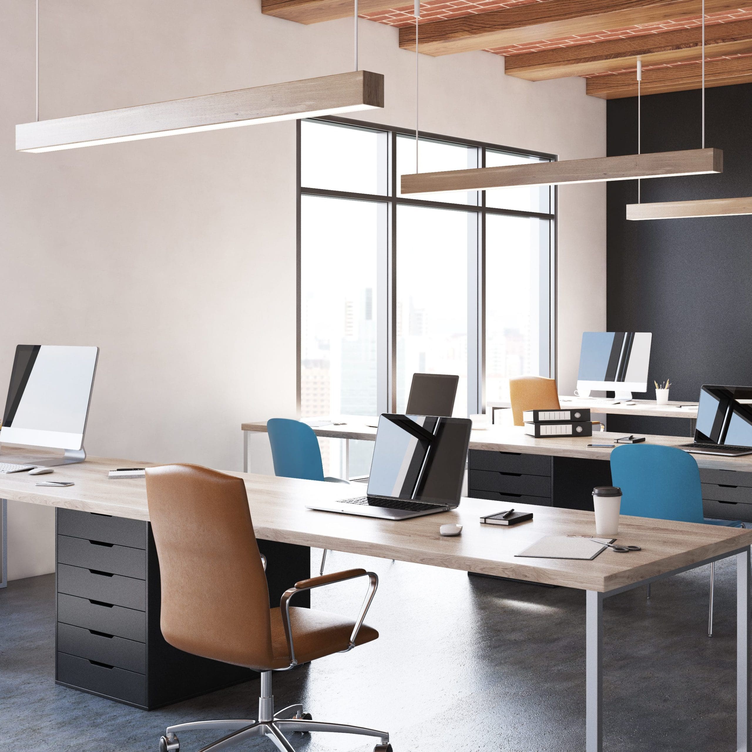 A modern office space with large windows, natural light, and exposed wooden beams on the ceiling. It features several workstations with computers, chairs, notepads, and coffee cups. The decor is minimalistic with neutral tones and a mix of brown and blue chairs.