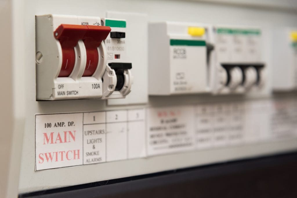 Close-up view of a control panel featuring labeled switches, including a prominent red and white switch labeled "MAIN SWITCH" and other smaller switches labeled for various functions such as "UPSTAIRS LIGHTS & SMOKE ALARMS.