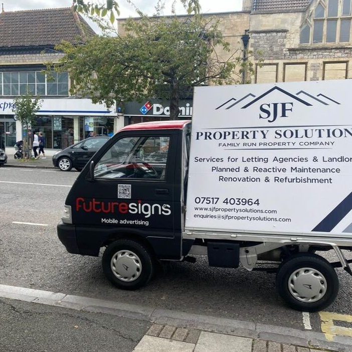 A small advertising vehicle with a sign "SJF Property Solutions" parked on a street. The sign lists services including letting agencies, landlords, maintenance, renovation, and refurbishment. Nearby is a Tesco express, Dominos, cars, and a "Futuresigns" ad.