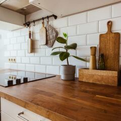 A modern kitchen with a wooden countertop, white subway tile backsplash, cutting boards, a potted plant, a salt shaker, and an induction cooktop. Kitchen utensils and a pot holder hang on the wall.